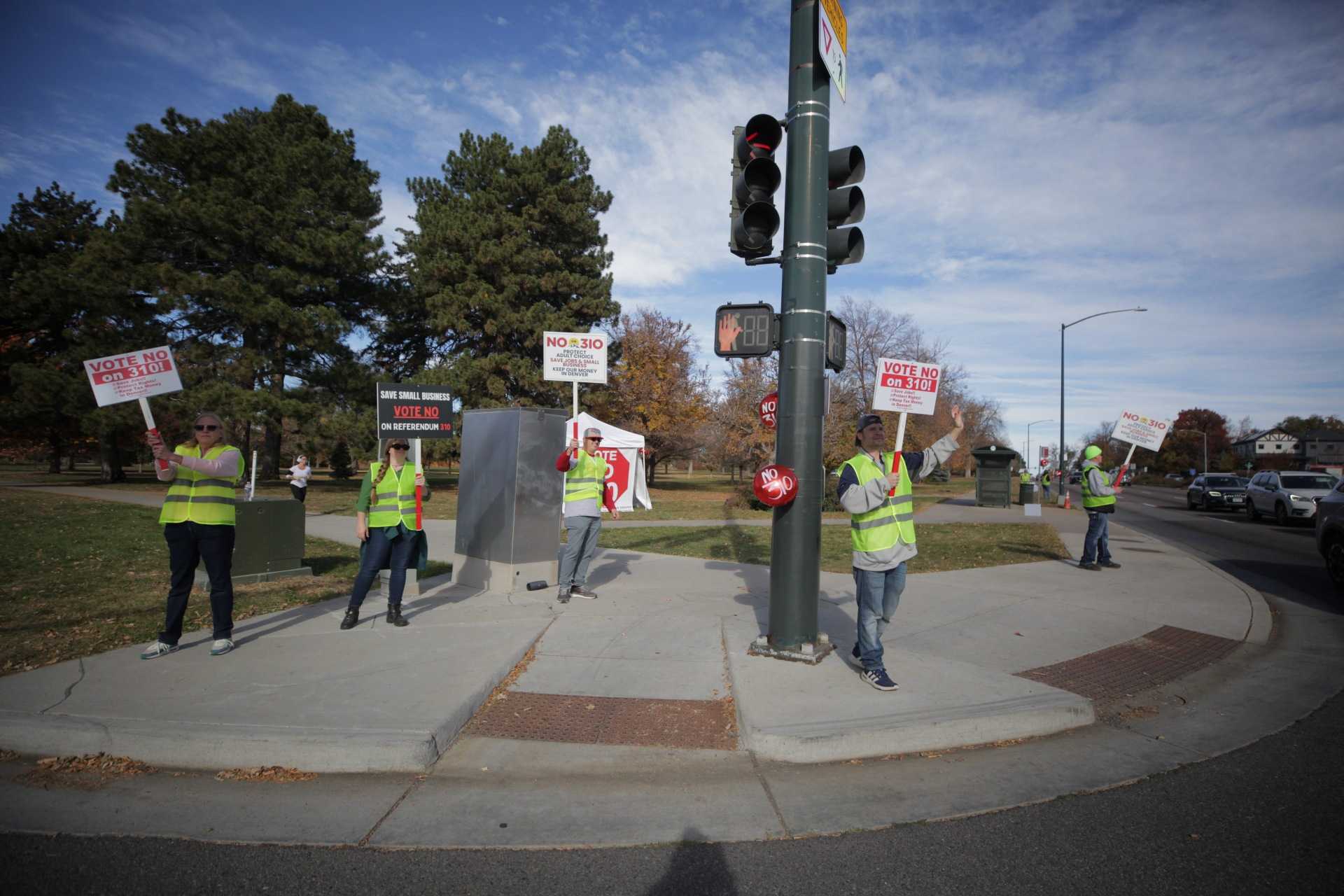 People in yellow safety vets hold "No on 310" signs on a street corner.