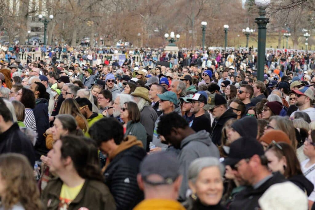 Thousands of people stand amid metal lamp posts in a park.